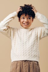 Young african american boy in stylish white sweater and brown pants expressing surprise against simple beige background