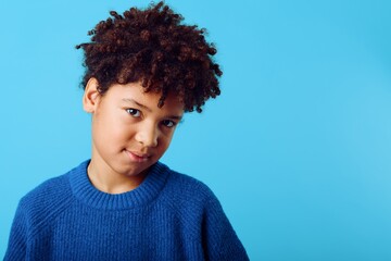 Young african american boy with curly hair wearing a blue sweater, standing against a matching blue background