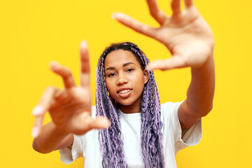 cheerful african american woman with colored dreadlocks showing and holding empty hands over yellow...