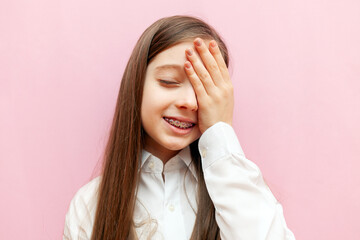 excited teenage girl is worried and shows a facepalm on a pink isolated background, an unhappy...
