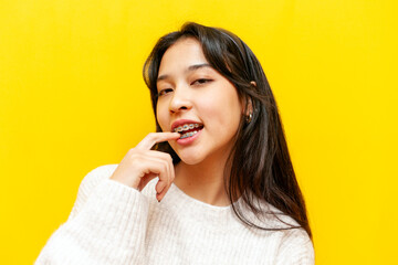 young pensive asian girl with braces flirts and thinks sexually over yellow isolated background, excited korean girl dreams and imagines and bit a finger