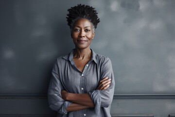 Portrait of a satisfied afro-american woman in her 50s with arms crossed in front of bare...