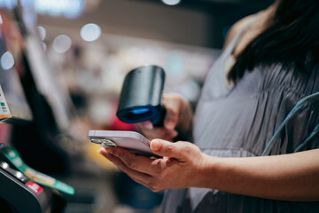 A close-up of a pregnant woman using her smartphone to make a payment, scanning and paying a bill...