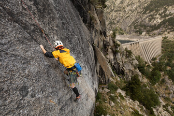 A man is climbing a rock wall with a yellow jacket on