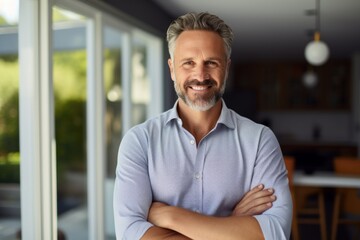 Fototapeta premium Portrait of a satisfied man in his 50s with arms crossed over stylized simple home office background