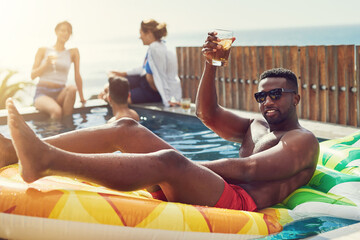 Man, toast drink and float in swimming pool with sunglasses, cheers and happy on rubber inflatable....