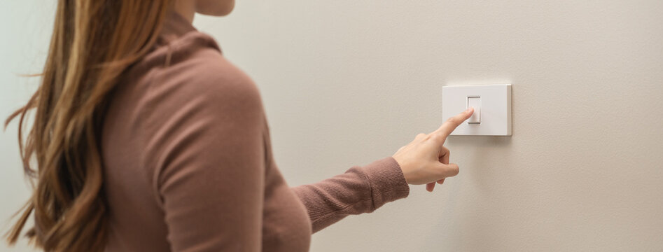 Asian young woman hand turn off on lighting switch at home room. Finger pushing light switch turn on or off white switch on wall for saving, control power electrical energy, eco environment concept.