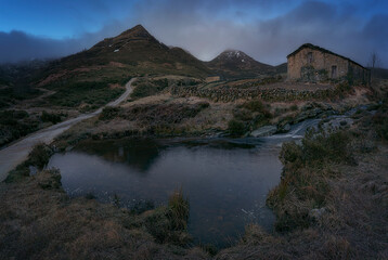 warm sunrise at the Pardo waterfall, in the mountain pass of Estacas de Trueba, Burgos, with a small pond in the foreground and a pasiega cabin between mountains