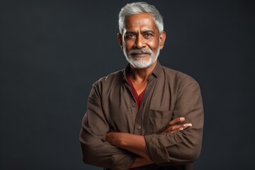 Portrait of a blissful indian man in his 60s with arms crossed over plain cyclorama studio wall