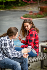 A young couple sitting on a bench using their smart phones; Bothell, Washington, United States of America