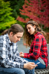 Obraz premium A young couple sitting on a bench using their smart phones; Bothell, Washington, United States of America