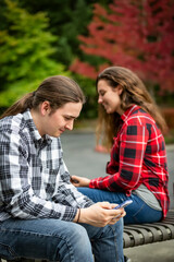 Fototapeta premium A young couple sitting on a bench using their smart phones; Bothell, Washington, United States of America