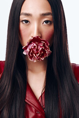 Beautiful woman with long black hair wearing red leather jacket posing with flower in mouth