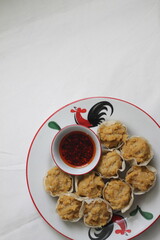 Chicken dumplings and a bowl of chilli oil on white plate decorated with cocks drawing or ayam jago in Indonesia. On white tablecloth. Selective focus