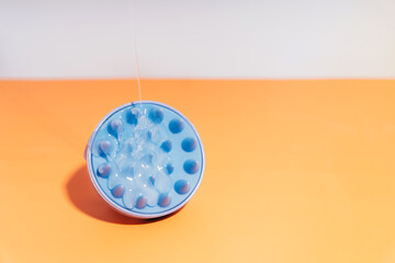 A shampoo on the orange pours on a blue massager for the head.