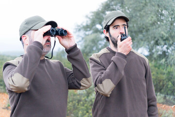 Two male rangers working in nature with walkie-talkies and binoculars 