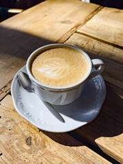 A beautifully crafted latte with intricate latte art, served in a classic white ceramic cup on a rustic wooden table. Perfect for coffee shop promotions and beverage presentations.