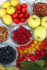 Apples, lemons, bananas, berries, carrots, leek, tomatoes, radishes, spinach and various nuts on white background. Healthy seasonal fruit and vegetable. Selective focus.