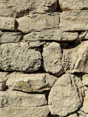Masonry wall of old stone blocks of limestone. Background texture of wild calcareous stone, irregular shape, stonework. Full frame. Vertical photo. Selective focus.