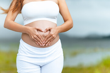 parenthood, mother, pregnancy, motherhood, constipation, illness, stomach, parent, femininity, touching. A woman is holding her stomach in the shape of a heart. love and care for the unborn child.