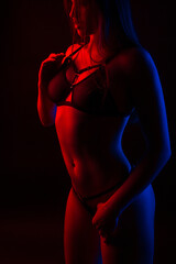 Sexy young brunette woman in black lingerie showing her slim attractive body in studio in colored light on a dark red background