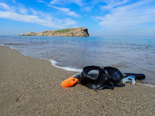 Obraz premium Scuba diving and snorkeling. Snorkel on sand beach In background is an island, Diving Goggles and Snorkel Gear stone near beach, Swimming equipment at Mediterranean sea beach in Jijel, Algeria, Africa
