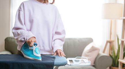 maid, housekeeping, hygiene, laundry, garment, steam, housewife, house, comfortable, clothes. A woman is ironing a shirt on an ironing board. The iron is hot and steam is coming out of it.