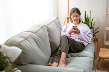smartphone, relaxation, communication, comfortable, message, living, chat, social, sofa, network. A woman is sitting on a couch and looking at her smartphone. She is wearing a pink sweater.