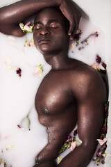 Flowers, relax and black person in milk bath for smooth, clean and hydrated body care routine. Calm, spa and African man wash in water with dairy liquid and floral plants for soft skin treatment.