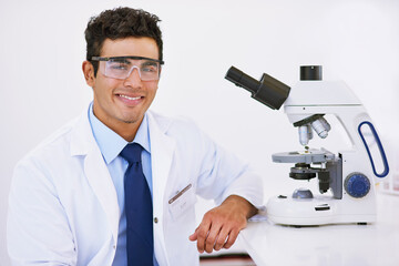 Scientist, man and microscope in portrait with smile, safety goggles and studying in laboratory for bacteria evolution. Person, technician and happy with tools for zoom, analysis and DNA research