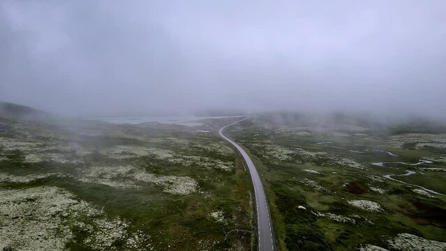 Drone Aerial View: Flying over a road, car and camper eventually enter the scene through the mist-covered tundra landscape in Rondane National Park, Norway.