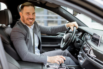 Smiling businessman driving luxurious car through city streets on a sunny day
