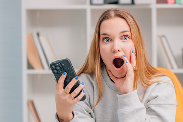 young blonde woman or student with blue eyes with mobile phone and surprised expression