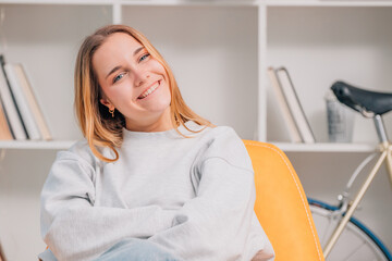 smiling blonde young woman sitting on sofa at home looking at camera happy