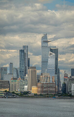 Obraz premium New York, NY, USA - August 1, 2023: W 29th street and north urban jungle under blue cloudscape. Hudson river in front. 30 Hudson yards dominate, Green tree line