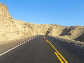 Asphalt road without people in desert towards the horizon with blue sky. Travel and freedom concept