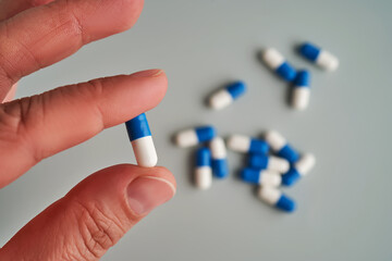 A hand holds a white and blue pill on a blue background.