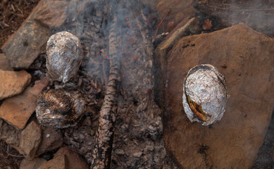 Smoke, a smoldering fire and potatoes wrapped in cooking foil. The atmosphere of field kitchen and simple camp food