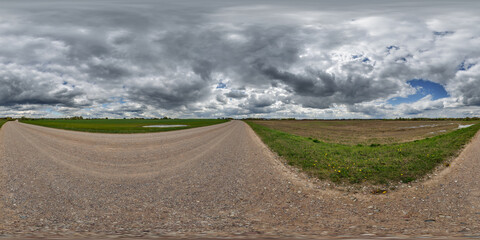 hdri 360 panorama on wet gravel road among fields in spring nasty day with storm clouds before...