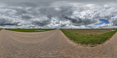 hdri 360 panorama on wet gravel road among fields in spring nasty day with storm clouds before sunset in equirectangular full seamless spherical projection, for VR AR virtual reality content