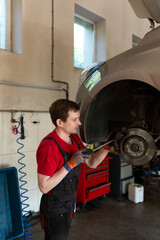 a mechanic stands by a car in a car service center. master repairs car brake discs and pads