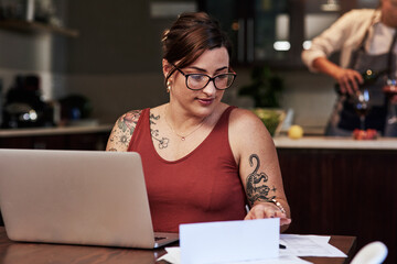 Home, laptop and check of paperwork, woman and reading of documents for bills, debt and mortgage. House, loan and person with computer, finance and budget for business, report and online with tattoo