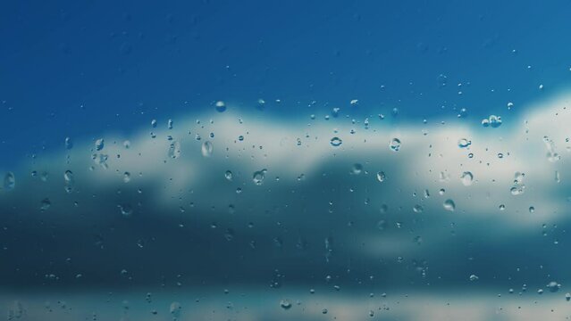 Time lapse foggy glass and raindrops. Horizontal fluffy clouds fly quickly across blue sky. Real time movement of clouds. Early morning. Sunlight is low from the side. Light vapors and humidity
