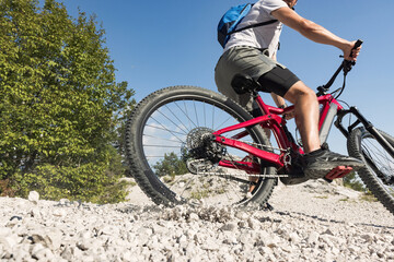 Mountain bike rider riding an electric bike along a white gravel trail on a sunny summer day. Outdoor sports activity concept.