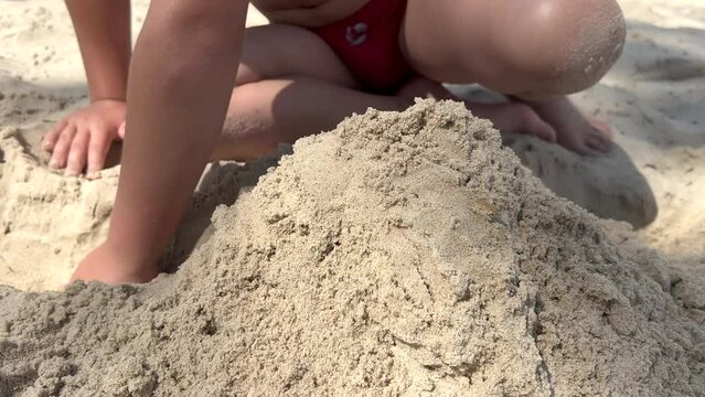 Hands little blonde boy playing with sand on beach ocean sea. Child building sand castle house. Family summer holidays and trips to warm countries