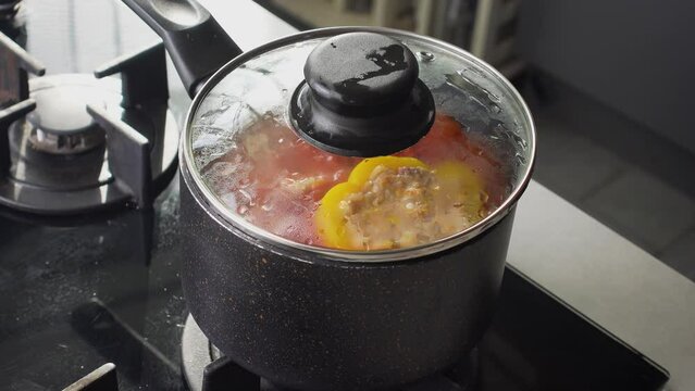 Stuffed peppers with meat and rice cooking in a pot on the stove in red tomato sauce. Sauce is bubbling and steaming, creating a delicious and appetizing food scene. 