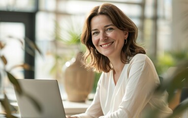 A smiling woman with brown hair at a laptop in a modern office. - Powered by Adobe