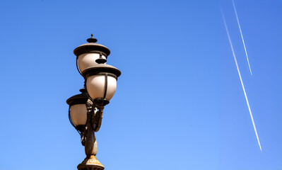 Street lamp made of three classically shaped glass spheres against a blue sky crossed by the...