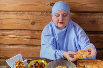 A Muslim woman in a blue hijab at the Eid al Fitr table takes a flatbread
