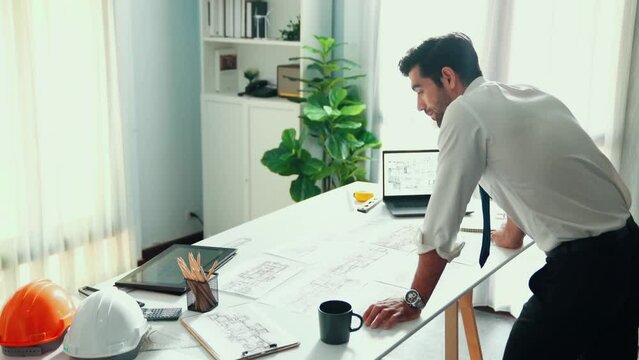 Architect engineer using laptop planning house design at office while sitting at meeting table with blueprint and equipment scatter around.Skilled civil engineer working at blueprint. Alimentation.